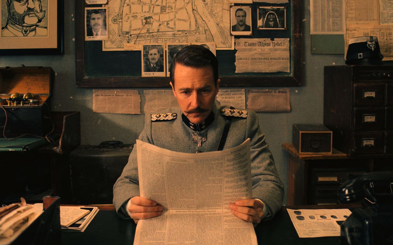 Edward Norton as Henckels reading the paper in The Grand Bud