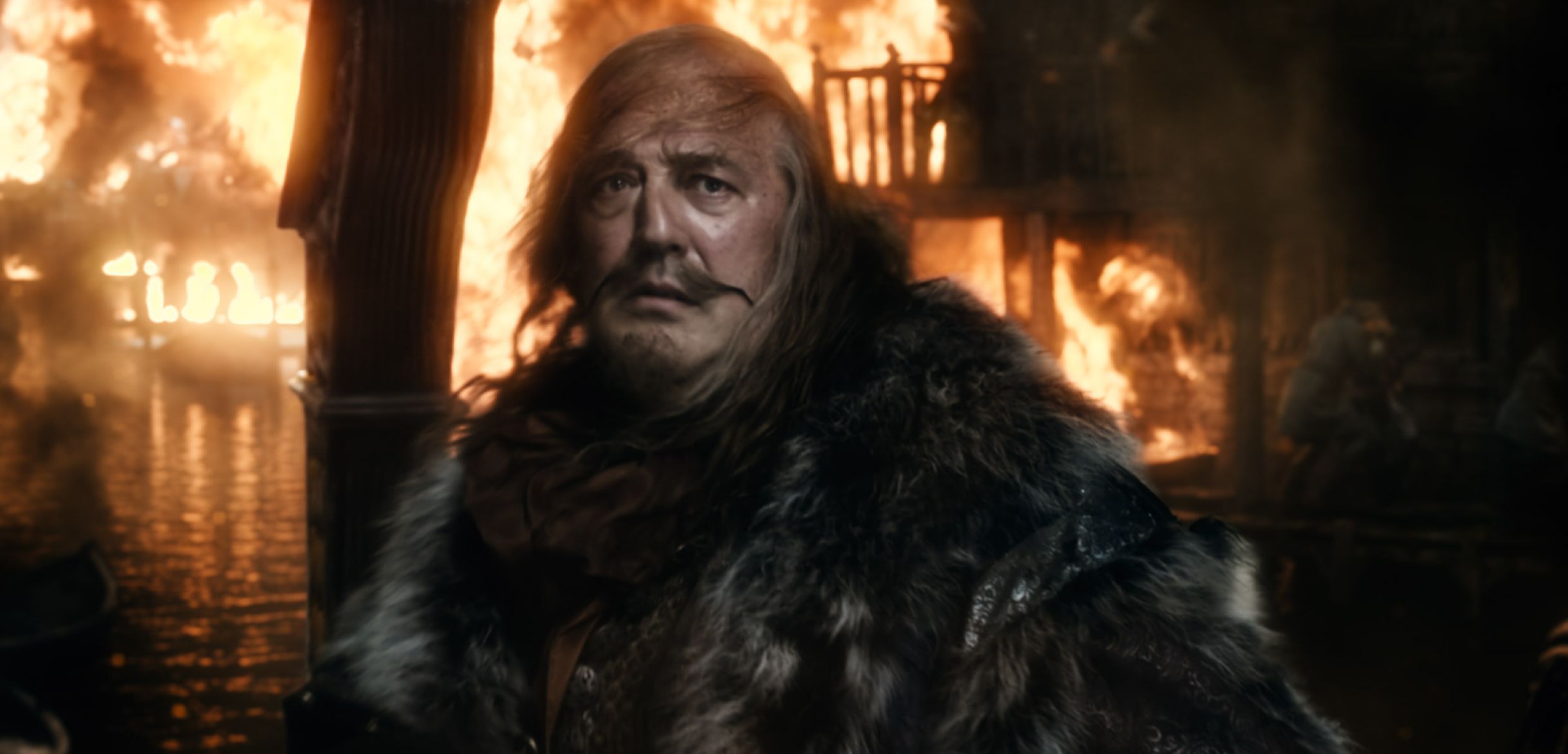 Stephen Fry as the Master of Laketown in front of burning ci